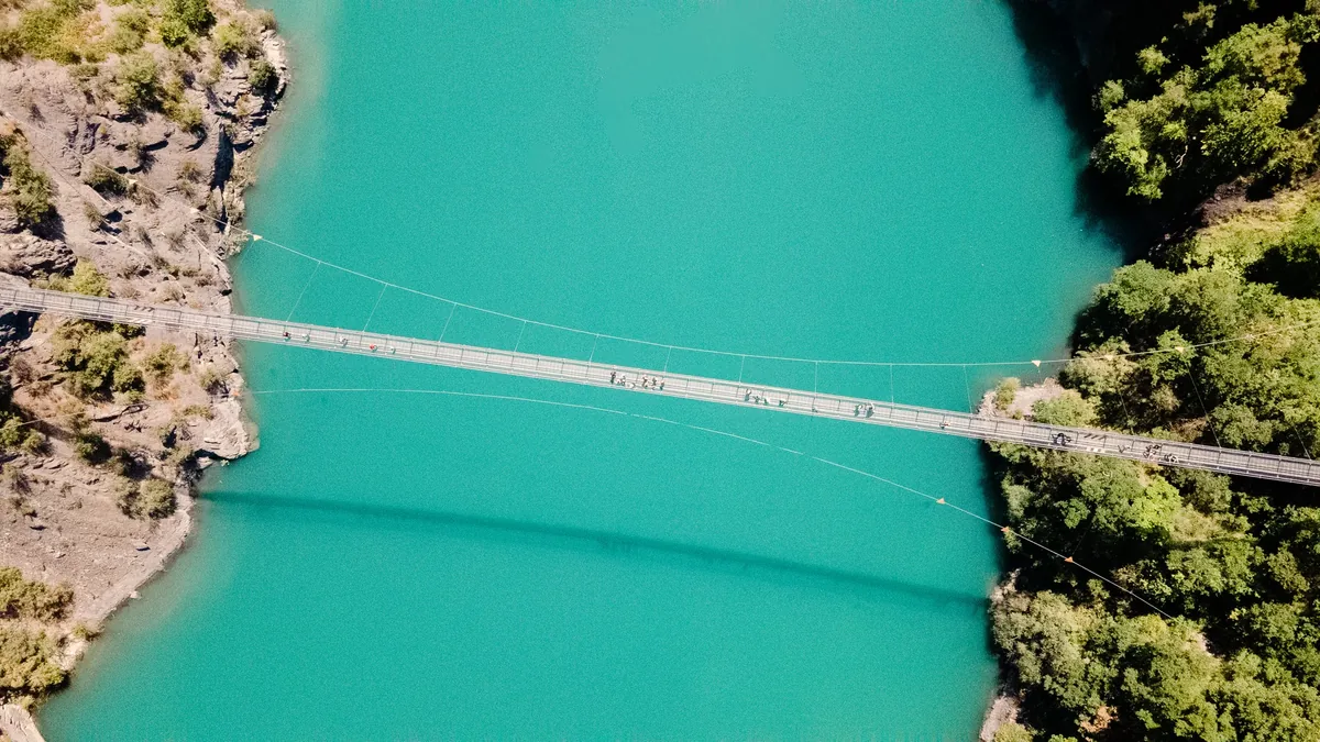 Vue aérienne d’une passerelle suspendue au-dessus de l’eau turquoise de Monteynard.