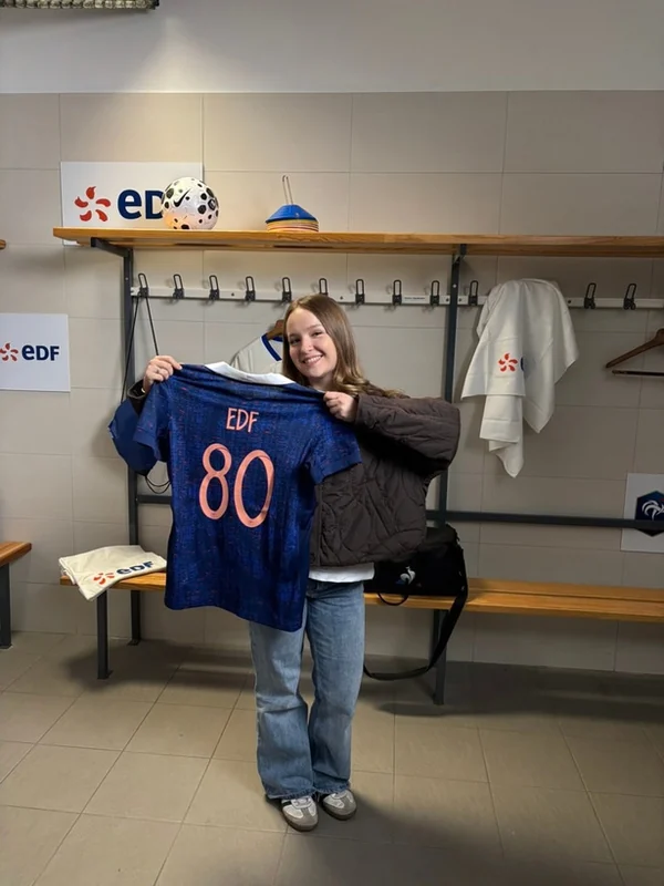 Luna Valy Estay tenant un maillot bleu EDF dans le vestiaire de l’Équipe de France.